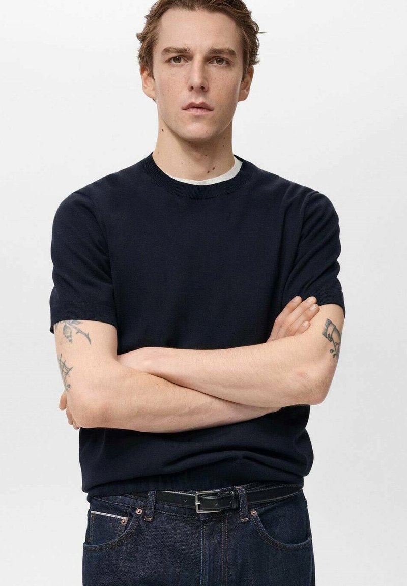 Námořnická modrá triko s krátkým rukávem a kulatým výstřihem, vyrobené z měkké látky, s kontrastním bílým vnitřním límečkem, nošené s tmavými džíny.
