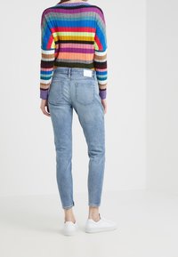 Niebieskie dżinsy o slim fit i lekko zwężających się nogawkach, zestawione z kolorowym, paskowanym swetrem z prążków i białymi sneakersami.