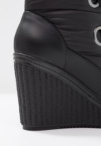 Bota negra de tacón cuña con parte superior de tela texturizada y detalles en cuero liso. Costuras destacadas y herrajes metálicos realzan el diseño.