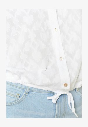 Blusa blanca de botón con textura floral, presenta botones perlados, dobladillo atado, combinado con jeans de mezclilla azul claro.