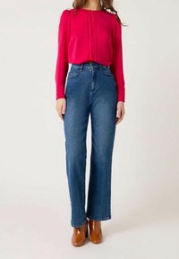 Red long-sleeve blouse with pleats, paired with high-waisted, straight-leg blue denim jeans. Brown heeled ankle boots.