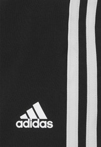 Tela negra con tres rayas blancas que corren verticalmente. Presenta un prominente logo blanco de Adidas en la esquina inferior izquierda.