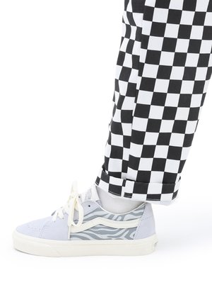 Grå og hvite joggesko med teksturert zebra-mønster og kremfargede lisser; paret med svart og hvit rutete bukser som viser detalj av avslutning.