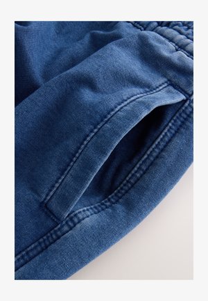 Mörkblå denimjoggers med mjuk textur, utrustade med elastisk midjeband och sidofickor. Sömmen är synlig längs kanterna.