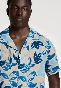 Kortärmad skjorta med en ljusblå bas och blå och beige blommönster, tillverkad av ett mjukt tyg med avslappnad passform och krage.