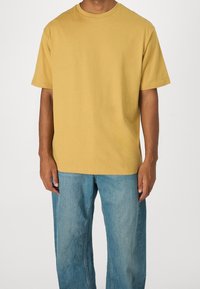 Camiseta de manga corta y cuello redondo en algodón amarillo mostaza, combinada con jeans de mezclilla azul claro de corte ancho. Diseño simple y casual.
