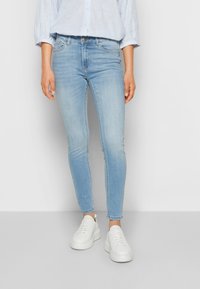 Jeans skinny azul claro feitos de denim, apresentando um design clássico de cinco bolsos e usados com ténis brancos.