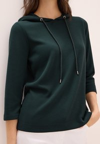 Dunkelgrüner Kapuzenpullover mit drei Viertelärmeln, gerippter Textur und verstellbaren Kordeln mit silbernen Akzenten. Lässige Passform und entspanntes Design.