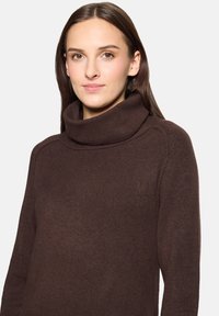 Pull en tricot marron avec un col bénitier haut, des manches longues et une finition texturée. Tissu doux et d'épaisseur moyenne.