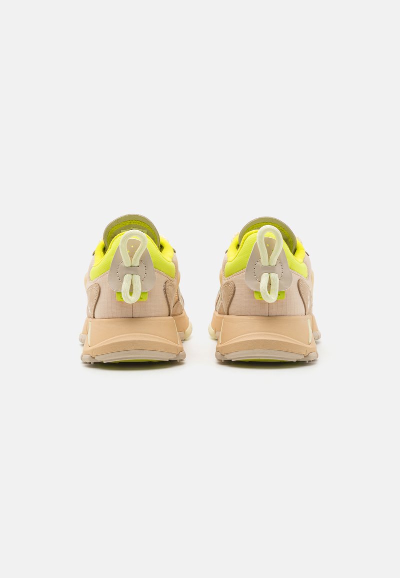 Sneakers w kolorze beżowym i żółtym, z fakturowaną cholewką, wyściełanym kołnierzem oraz charakterystycznymi pętlami na pięcie.
