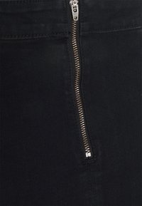 Svart denimtyg med en synlig dragkedja i guldfärg. Slät textur, figursytt utförande och minimalistisk stil utan ytterligare utsmyckningar.