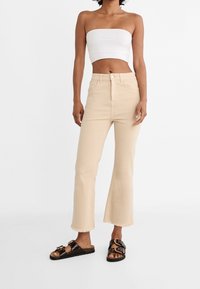 Mujer que lleva un top blanco sin mangas, jeans cortos de tiro alto en color beige con bajos desgastados, y sandalias negras con hebillas dobles.