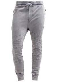 Světle šedé joggingové kalhoty vyrobené z měkké tkaniny, s žebrovanými kolenními panely, elastickým pasem a přiléhavými manžetami na kotnících.