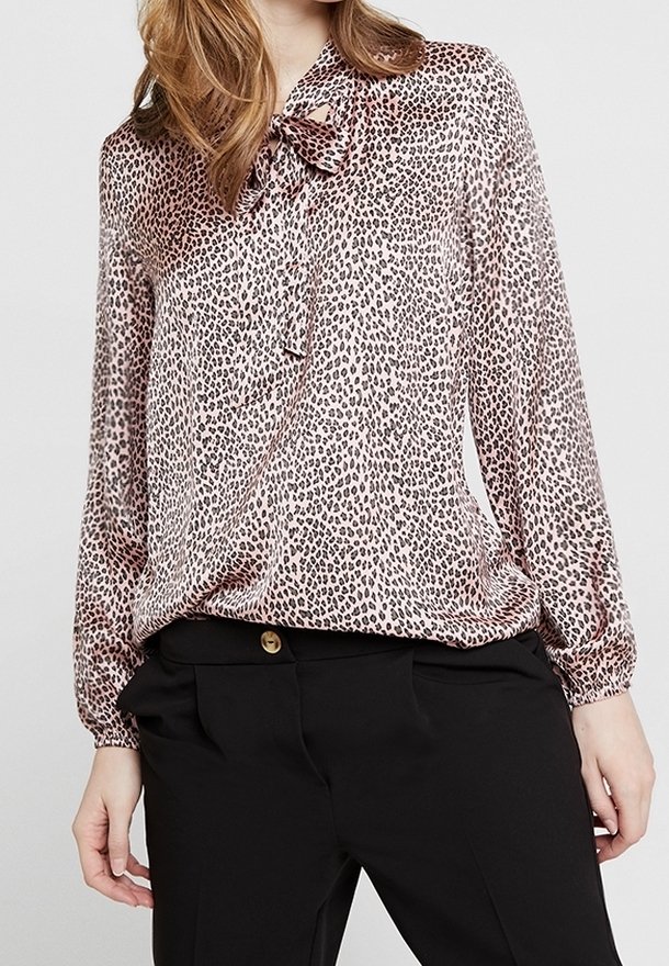 Blouse en imprimé léopard en tissu léger avec un nœud au col. Manches longues avec des poignets froncés. Associée à un pantalon noir.
