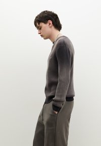 Donkergrijze ribbeltrui met een geleidelijke ombre-effect, gecombineerd met olijfgroene joggers; de trui heeft een ronde hals en smalle manchetten.
