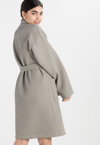 Grå badekåpe med vaffelmønster, belte, vide ermer og sidelommer, med en løs passform og kne-lengde design.