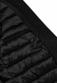 Giacca a vento nera con texture trapuntata, tasca con zip e bottoni. Composta da materiali lucidi e opachi, presenta un design slanciato.