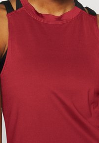 Rood atletisch tanktop met een gladde textuur, ronde hals en zwarte bandaccenten. De stof lijkt lichtgewicht en flexibel.