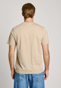 Bežinė medvilninė marškinėlių su apvalia iškirpte su trumpomis rankovėmis, vienodai nuspalvinta, prigludusi forma ir tiesiais kraštais. Dėvimi su šviesiai mėlynais džinsais.