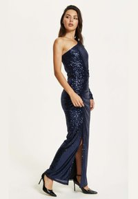 Navy blue sequin evening gown with one shoulder, fitted silhouette, and thigh-high slit. Paired with black high heels. Smooth texture.