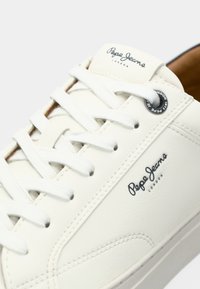 Gros plan d'une basket blanche Pepe Jeans London montrant les lacets, les détails cousus et le logo de la marque sur la languette et le côté.