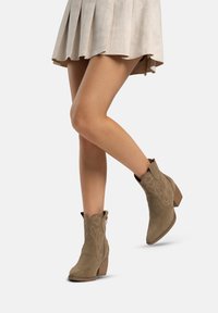 taubefarbene Wildleder-Ankle-Boots mit bestickten Details und einem gestapelten Absatz, kombiniert mit einem plissierten beigen Rock.