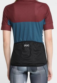 Lyhytsleeve pyöräilypusero, jossa on viininpunainen yläosa, teal-välinen osa ja musta alaosa, tekstuurinen kangas ja takatasku.