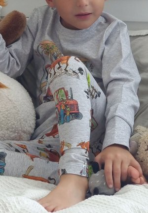 Harmaa puuvillapaita-setti, jossa on eläin- ja traktori-kuvioita. Pitkät hihat ribba-reunuksilla ja kuviolliset housut. Lapsi istuu sängyssä.