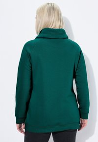 Felpa teal con colletto alto e polsini e orlo a costine. Tessuto morbido; presenta maniche raglan. Stilizzata senza hardware o accenti visibili.