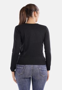 Maglione nero a maglia con maniche lunghe, vestibilità slim, scollatura rotonda e orlo a coste. Abbinato a jeans in denim blu con tasche posteriori.