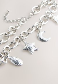 Chunky silver chain bracelet with star, crescent moon, and teardrop-shaped charms on a light background.