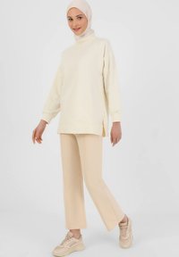 Cream-colored sweatshirt with long sleeves and side slits paired with light beige wide-leg pants and tan sneaker shoes. Smooth texture.