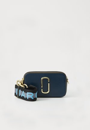 Bolsa retangular cruzada azul-marinho com logo duplo em ouro e alça preta, apresentando texto azul e cinza sobre fundo branco.