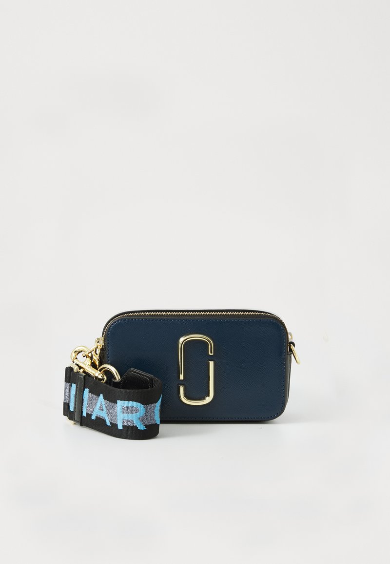 Bolsa retangular cruzada azul-marinho com logo duplo em ouro e alça preta, apresentando texto azul e cinza sobre fundo branco.