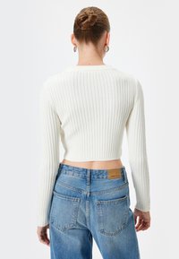 Maglione bianco a coste corto con maniche lunghe, abbinato a jeans in denim blu a vita alta con etichetta in pelle sul retro.