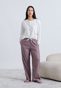 Balta, garām piedurknēm top ar pogu iesplēgumu, kopā ar svītrainām, brīvi pieguļošām biksēm rozā un bordo toņos, ar elastīgu jostasvietu.