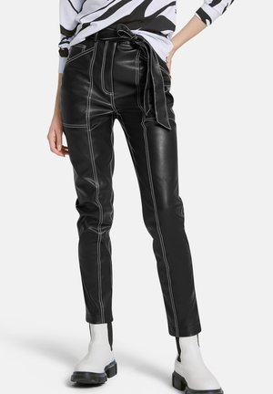 Zwarte leren broek met witte stiksels, met een hoge taille, riemstrik en taps toelopende benen. Gecombineerd met witte enkellaarsjes.