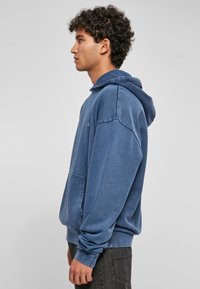 Felpa blu in cotone con tasca frontale, cappuccio con cordino e dettagli del logo ricamati sul lato sinistro. Vestibilità comoda e polsini a coste.