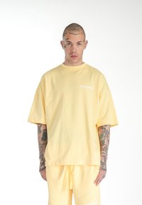 Gul oversized kortærmet t-shirt med rund hals, med et hvidt "MULTIPLY" logo på brystet. Blød bomuldsstof.