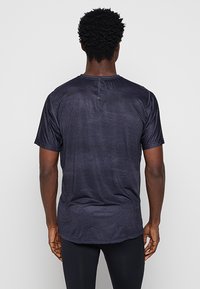 Granatowa koszulka z krótkim rękawem, wykonana z miękkiego materiału o delikatnym połysku, wyposażona w okrągły dekolt i zaokrąglony dół. Widoczna teksturowana powierzchnia.