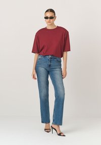 Burgundská oversized tričko spárováno se světle modrými rovnými džíny. Modelka nosí černé sluneční brýle a sandály na vysokém podpatku.