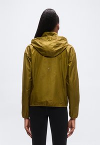 Chaqueta impermeable verde oliva con capucha, que presenta una textura suave, puños elásticos y un pequeño detalle reflectante en la parte trasera.