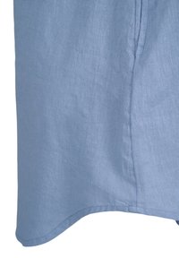 Tissu en lin bleu clair avec texture visible, montrant une couture latérale et une partie d'une poche sur un vêtement.