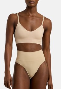 Beige bh med tunna band och en mjuk, slät yta. Matchas med högmidjade beige trosor, båda har minimalistiska mönster.