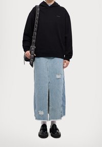 Felpa nera oversize con logo, abbinata a una gonna di jeans azzurri chiari con spacco frontale e dettagli strappati. Scarpe nere completano il look.