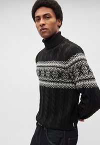 Čierny pletený sveter s rebrovaným rolákom, ktorý má na hrudi biely vzor Fair Isle a na tele textúru zošitého pásového pletenia.
