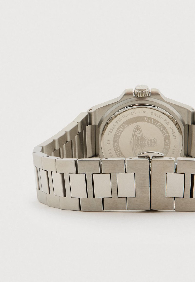 Edelstahl-Uhrenarmband und Gehäuserückseite mit graviertem Vivienne Westwood-Logo und Text, flach auf einer weißen Oberfläche liegend.