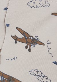Beige stof met een patroon van bruine vliegtuigen en blauwe wolken. De textuur is zacht met zichtbare stikdetails.
