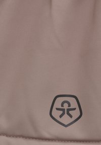 Texturerat rosa tyg med en svart logotyp i sköldform som föreställer en figur med utsträckta armar; designen är elegant och modern.