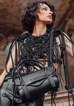 Černý top ve tvaru lana s propracovanými uzly, doplněný malou strukturovanou černou koženou kabelkou s zakřiveným klopovým víkem a dvojitými uchy.